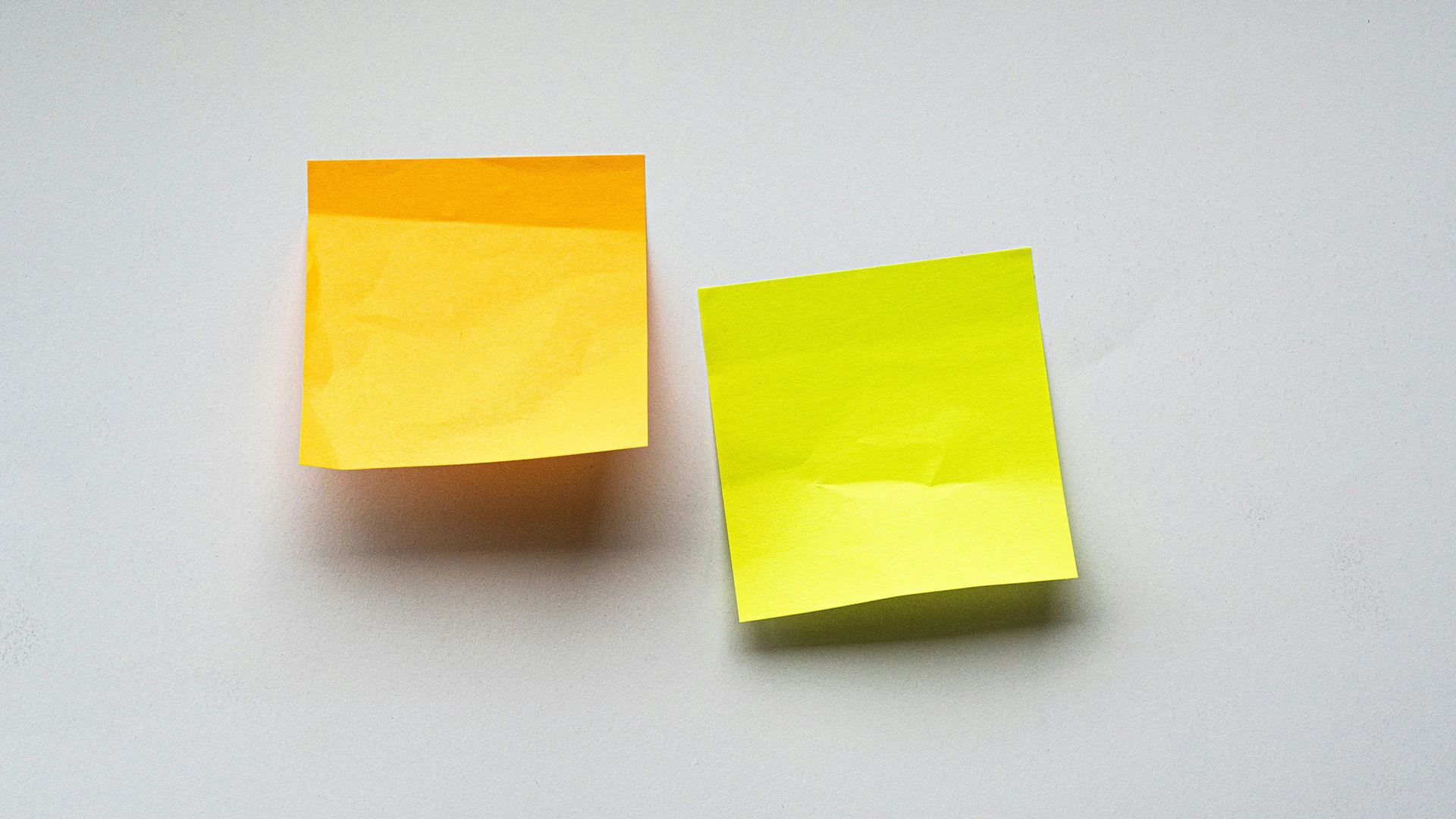 Two sticky notes, one yellow and one green, placed side by side on a light gray surface, representing brainstorming or planning.